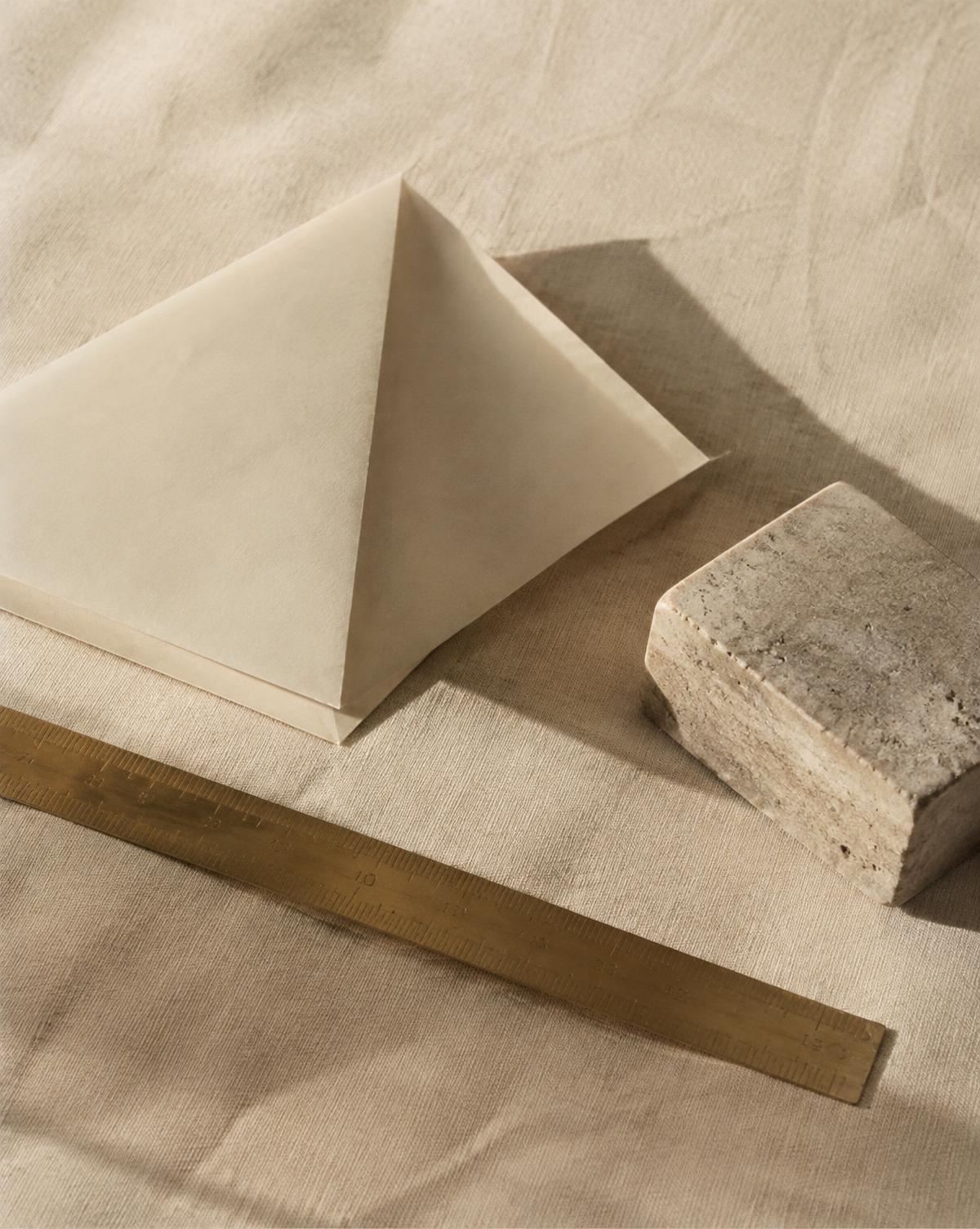 Folded paper, a bronze ruler and a stone block on ivory linen